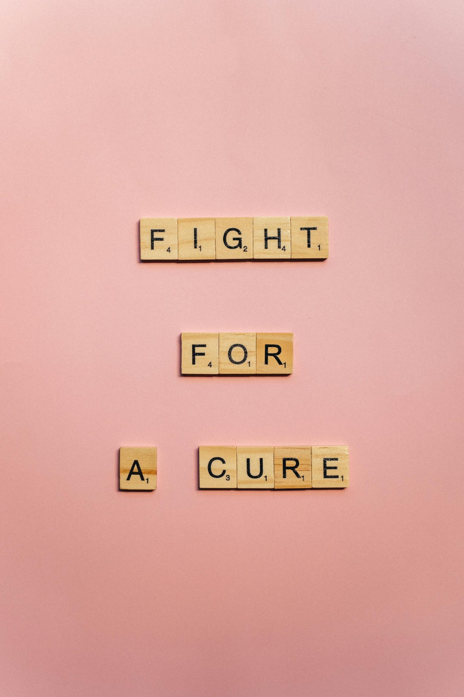 Wooden letter blocks spell 'Fight for a Cure' on a pink background promoting cancer awareness.